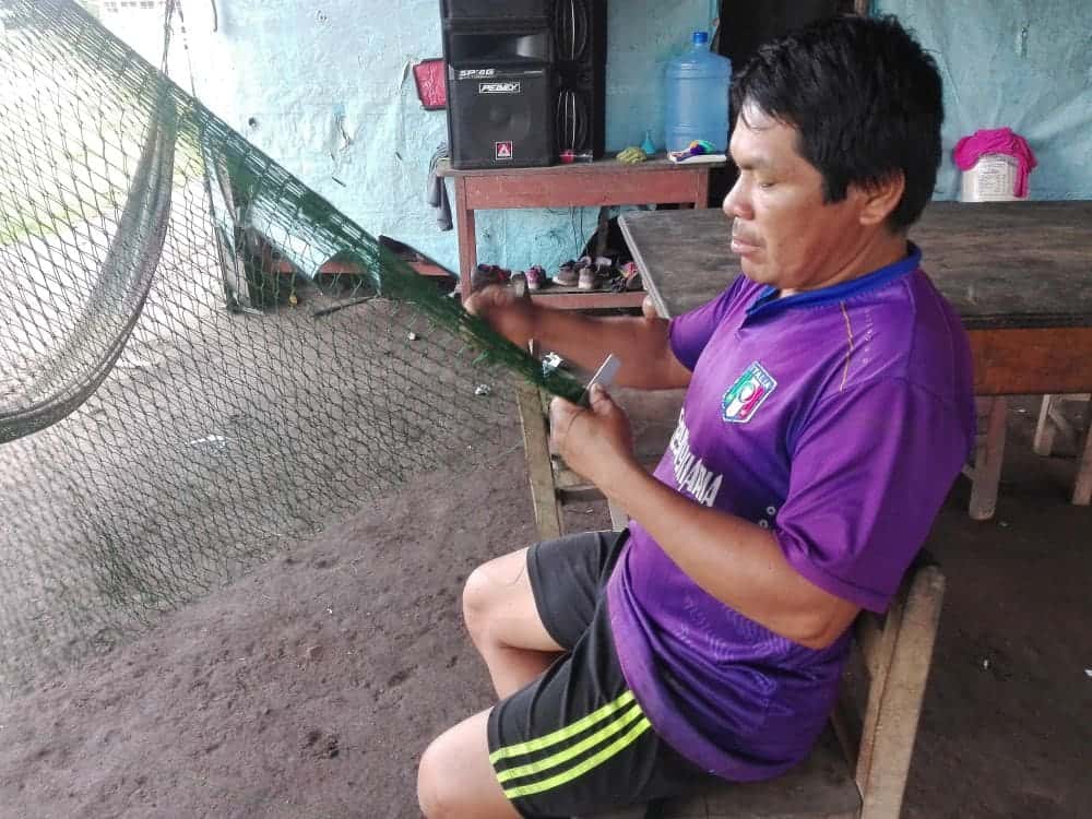 An experienced fisherman is knitting a fishing net. He will take us Nuevo Progresso in one hour 